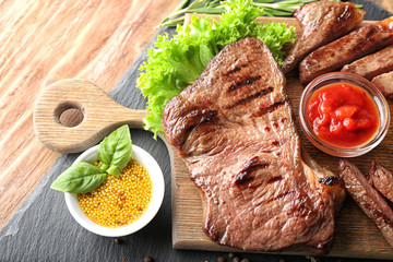 Board with tasty cut steak, herbs and sauces on wooden table