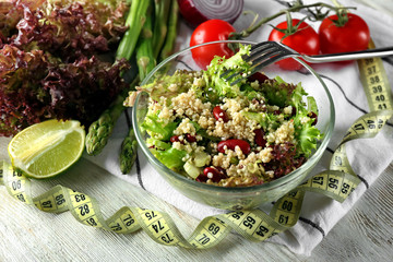Bowl with tasty quinoa salad and measuring tape on wooden table. Diet concept