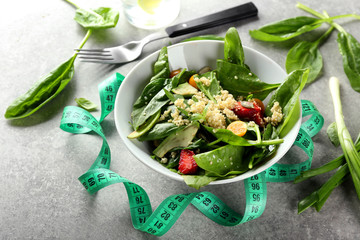 Bowl with tasty quinoa salad and measuring tape on table. Diet concept