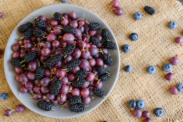 Fresh berries of blueberry, blackberry and gooseberry on a plate. It can be used as a background