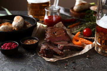 Glass of delicious beer with grilled steak and sausages on grunge table