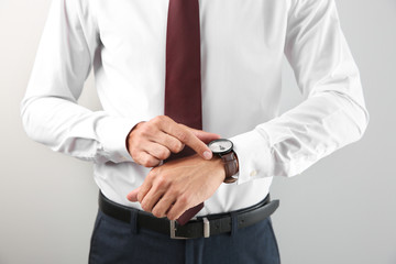 Obraz premium Businessman looking at his watch on light background. Time management concept
