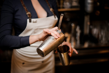 Bartender girl pourring a cocktail drink from one steel cup to another