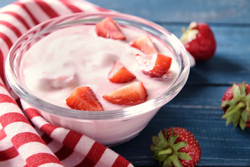Bowl with yogurt and strawberries on wooden table, closeup