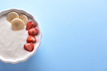 Bowl with yogurt, banana and strawberries on color background