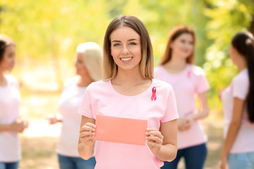 Beautiful woman with pink ribbon holding card outdoors. Breast cancer concept