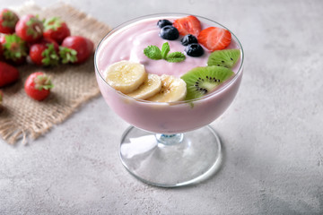 Glass bowl with strawberry yogurt and fresh fruits on grey background