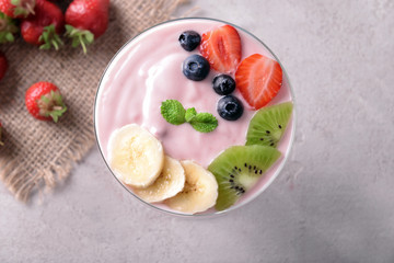 Glass bowl with strawberry yogurt and fresh fruits on grey background