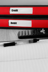 Red folders with credit and debit written on the label on a desk with selective colour