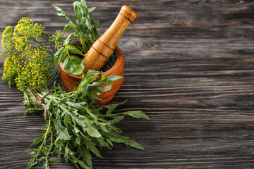 Different fresh herbs with mortar on wooden background
