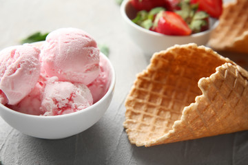 Bowl with tasty strawberry ice cream and cone on table, closeup