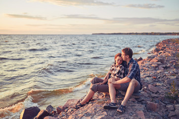 Lovers in a lake. Young couple in love sitting on the park ground near the water while these young man playing guitar in sunset time.