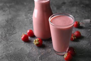 Glass and bottle with strawberry smoothie on grey table