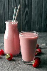 Glass and bottle with strawberry smoothie on grey table