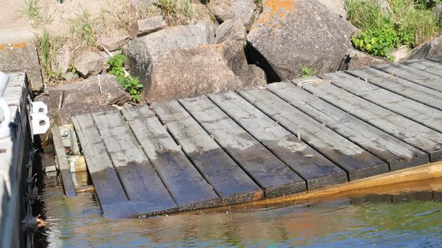 Unhooked wooden dock on the lake leaning on rocks. Dock waiting to be repaired as it bobs in the water.