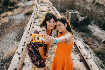 .Two young sisters enjoying a fun summer afternoon on abandoned train tracks, taking fun pictures together. Family vacation. Lifestyle.