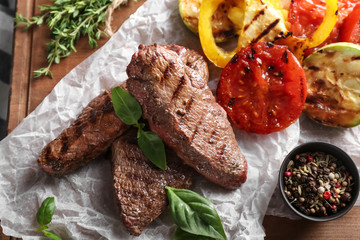 Tasty grilled meat with vegetables and spices on wooden board