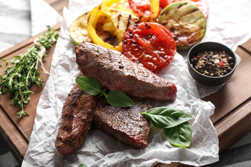 Tasty grilled meat with vegetables and spices on wooden board