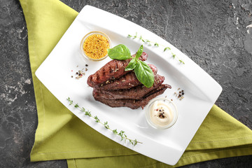 Tasty grilled meat with basil, sauces and spices on plate