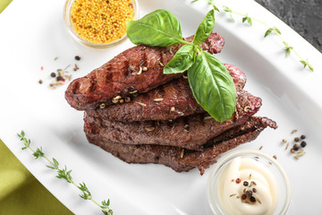 Tasty grilled meat with basil, sauces and spices on plate