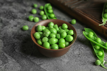 Bowl with green peas on grey table