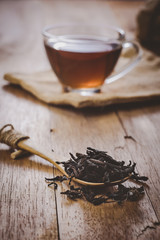 close-up dry chinese tea in wooden spoon on table, a cup of tea on sackcloth background, vintage tone