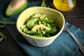 Bowl with green peas, cucumber and avocado on wooden table