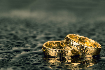 Wedding rings with water drops on dark background with copy space.