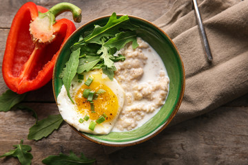 Bowl with tasty oatmeal and fried egg on wooden table