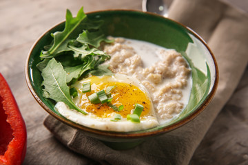 Bowl with tasty oatmeal and fried egg on wooden table