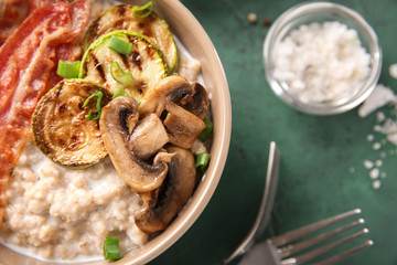 Bowl with tasty oatmeal, fried bacon, mushroom and squash on table