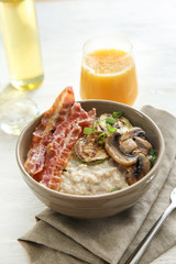 Bowl with tasty oatmeal, fried bacon, mushroom and squash on wooden table