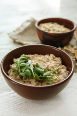 Bowl with tasty oatmeal and arugula on wooden table