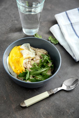 Bowl with tasty oatmeal, fried egg and arugula on table