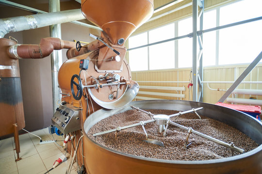 Background shot of modern drum roasting machine with fresh brown coffee beans in workshop of coffee processing manufactory