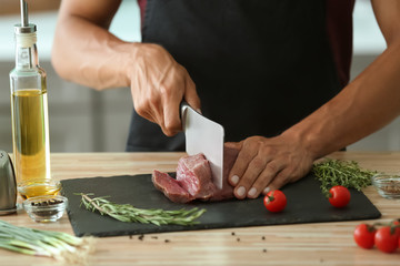 Man cutting raw meat on slate plate in kitchen