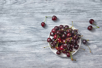 Ripe sweet cherry on a white plate on a gray wooden background. Place for text.