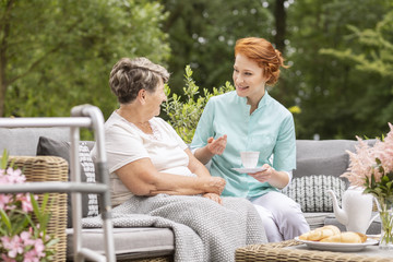 Smiling nurse talking with happy elderly woman during meeting on the terrace