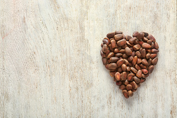 Heart made of tasty pine nuts on wooden background