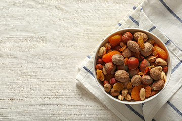 Bowl with different nuts and dried fruits on wooden background