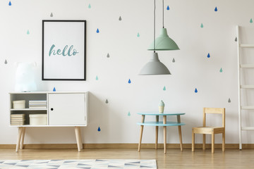 Real photo of a pastel blue and mint kid room interior with a poster above a white cupboard...