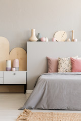 Pink pillows on grey bed with headboard in bedroom interior with rug and cabinet. Real photo