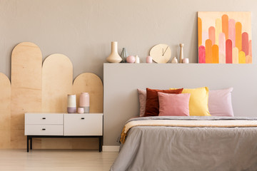 Colorful painting on grey bedhead of bed with cushions in bedroom interior with cabinet. Real photo