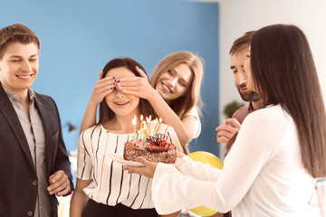 Happy colleagues presenting cake to young woman on her birthday in office