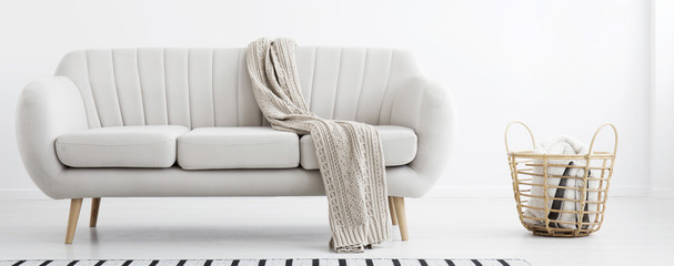 Blanket thrown on light grey sofa standing in the real photo of bright living room interior with...