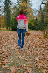 girl is walking in the autumn park.  tourist woman walks with a backpack over an autumn park with fallen leaves
