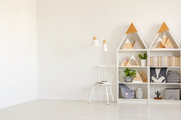 Real photo of white kid room interior with two lamps, mountain shape rack with books and decor and...