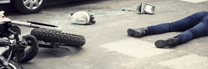 Fatal aftermath of a car accident concept - dead body and crashed motorcycle parts lying on the road