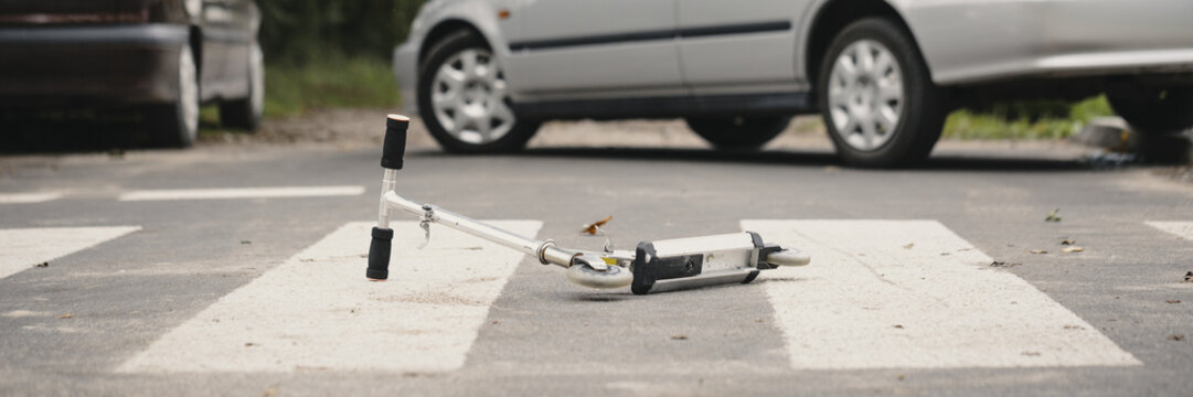 Drunk driving concept. Fatal aftermath of a car accident - a kid's scooter lying on an empty road with cars in the background