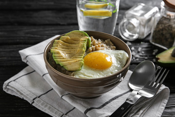 Bowl with delicious oatmeal, egg and avocado on wooden table
